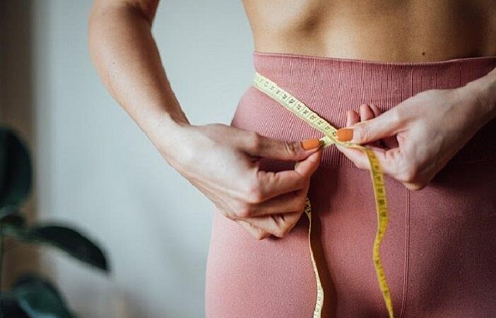 Frau mit niedrigem BMI misst ihren Bauchumfang mit einem Maßband.