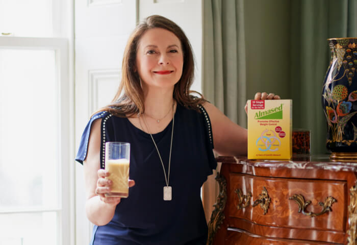 Olga mit Almased Portionsbeuteln und Almased-Shake im Glas berichtet von ihren Erfolgen