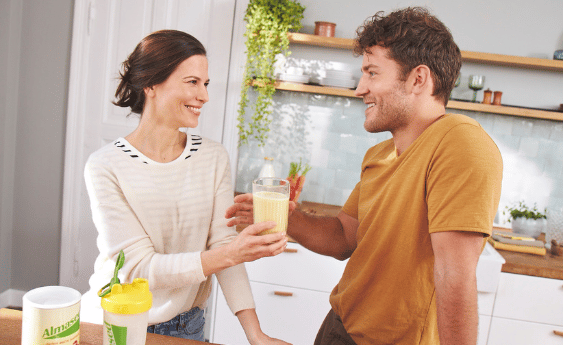 Paar steht in der Küche und teilt sich einen Almased Shake