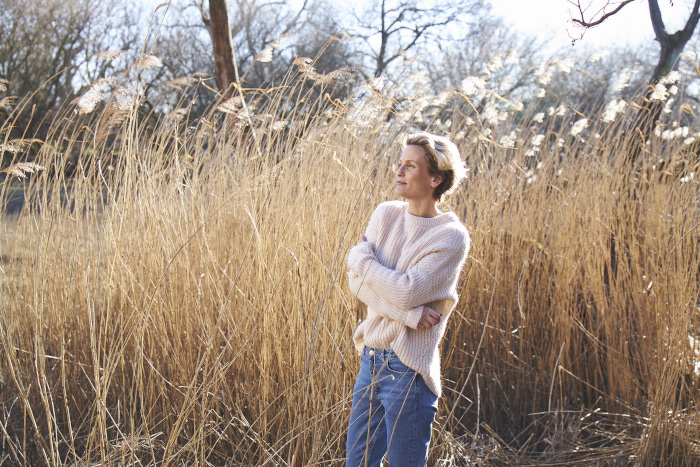 Frau steht im schulterhohen Seegrass mit gemütlichem Pulli und genießt die Sonne