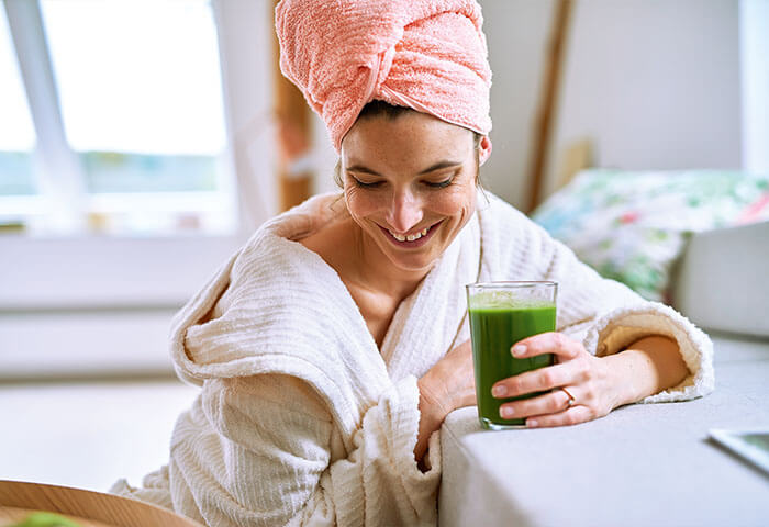 Frau im Bademantel trinkt glücklich grünen Shake zum Fasten