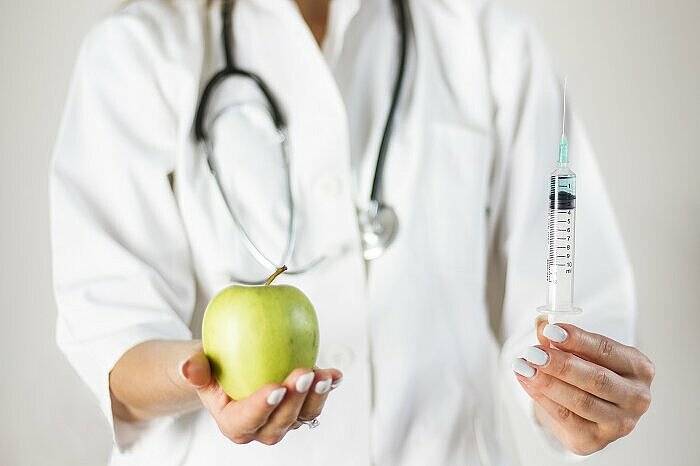 Ärztin hält einen Apfel der Abnehmspritze entgegen