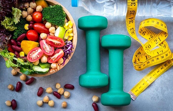 Schüssel mit Gemüse, Hanteln und Maßband auf einem Tisch, um den Effekt von glykämischen Index zu verdeutlichen