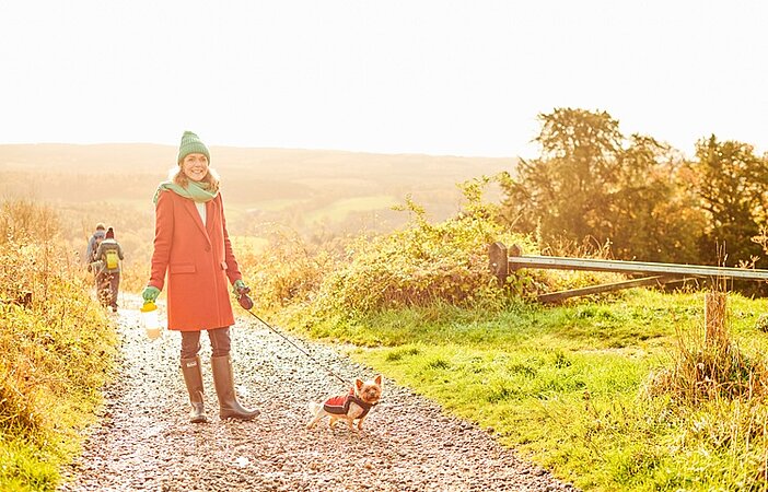 Frau-geht-mit-Hund-in-schoener-Natur-spazieren-Ablenkung-vom-Heisshunger