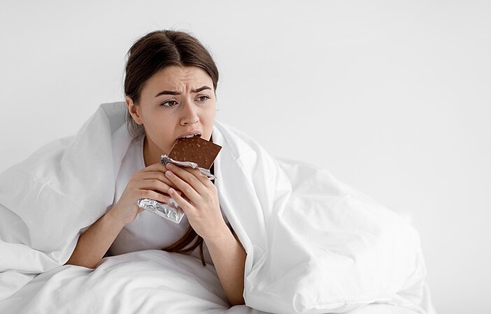 traurige-Frau-im-Bett-isst-eine-Tafel-Schokolade