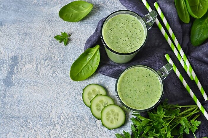 Grüner Abnehmshake mit Gurke, Spinat und grünen Strohhalmen in zwei Gläsern