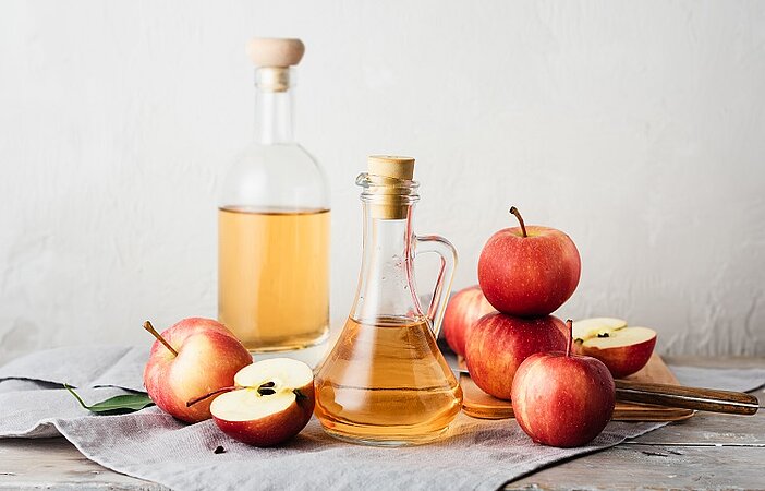 Zum Glukose-Trick gehört Apfelessig, der in einer Karaffe mit frischen Äpfeln auf einem Tisch angerichtet ist