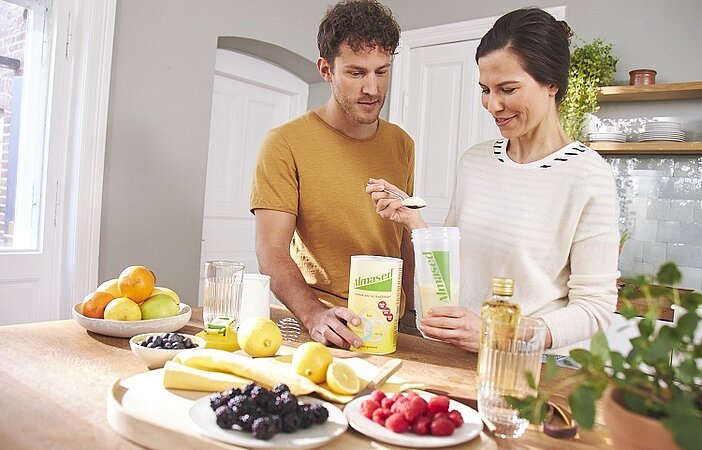 Paar in einer Küche mixt Almased Shake mit verschiedenen Zutaten, um eine hohe biologische Wertigkeit zu erreichen.