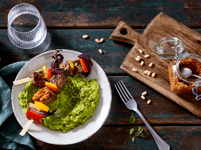 Diät Rezept für Bunte Lammspiesse auf Erbsen Minzpüreee mit Tomatenpesto auf rustikalem Holztisch mit weißen Teller serviert